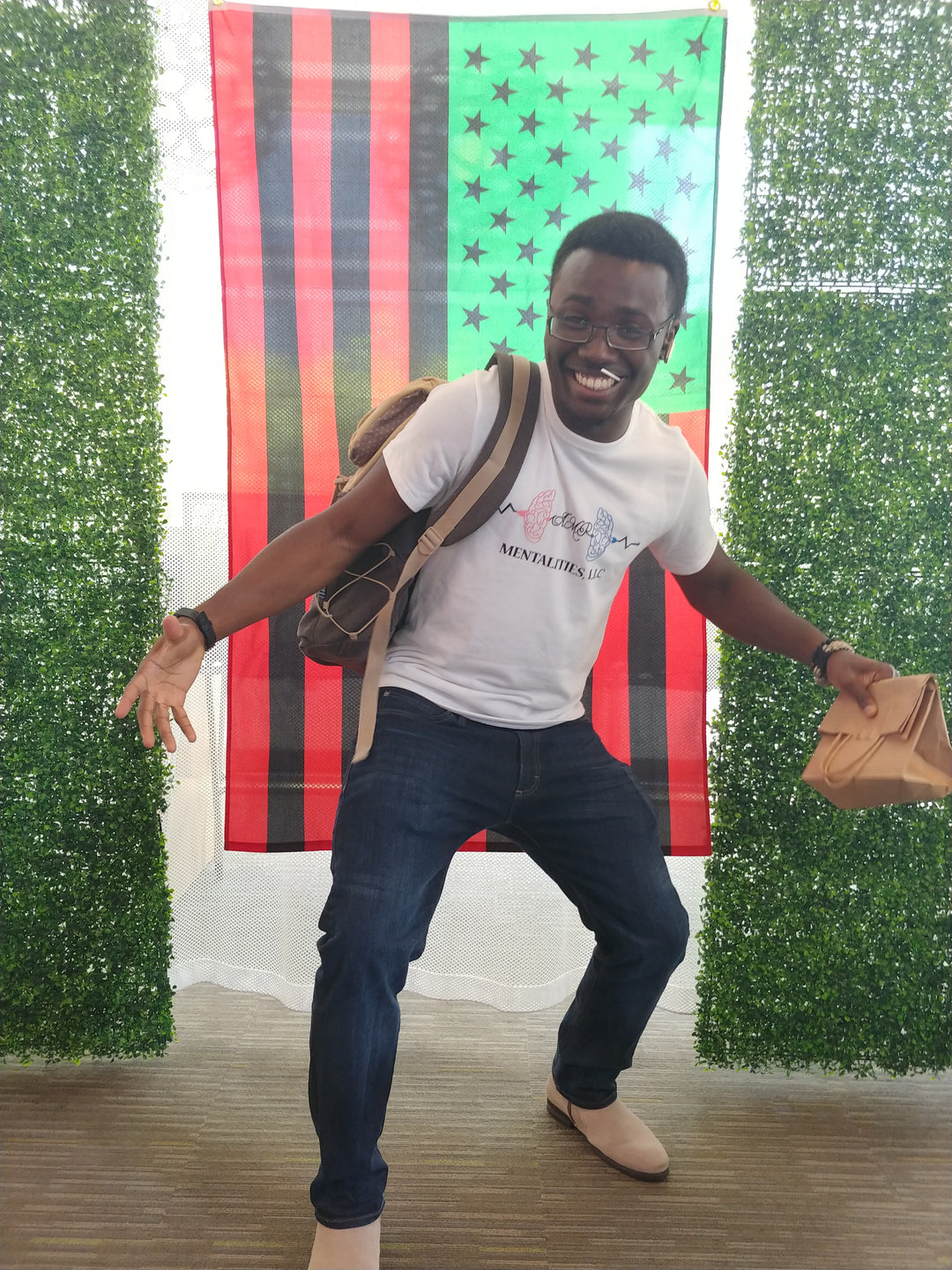 Founder, Marcus G. Vilmé, wearing the white "My Body Is My First Gym" Vintage T-Shirt. Smiling and posing with a lollipop in his mouth with the Pan Afro-American flag behind him.